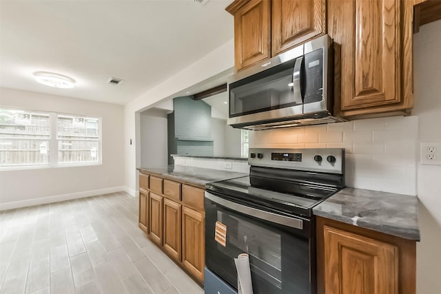 9096 N Comanche Cir, Willis, TX 77378 - kitchen featuring stainless steel appliances, brown cabinets, tasteful backsplash, baseboards, and dark countertops