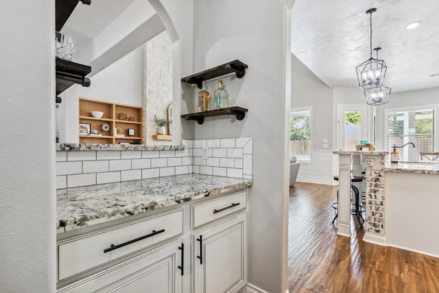 1935 Invermere Dr, Spring, TX 77386 - bar featuring dark wood-style floors, decorative backsplash, arched walkways, a chandelier, and hanging light fixtures