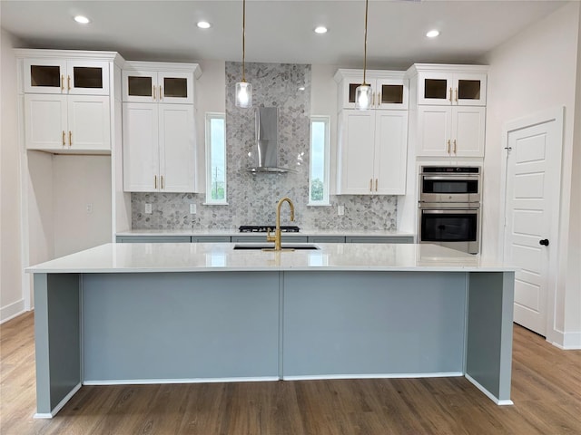 1307 71st St Unit A, Houston, TX 77011 - kitchen featuring wall chimney range hood, an island with sink, wood finished floors, tasteful backsplash, and white cabinetry