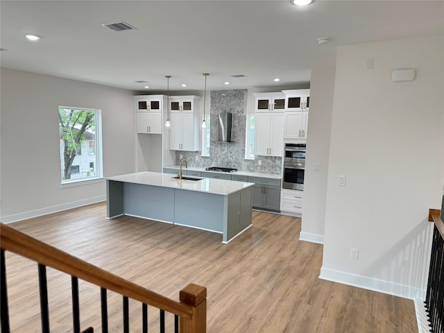 1307 71st St Unit A, Houston, TX 77011 - kitchen featuring wall chimney range hood, double oven, tasteful backsplash, a kitchen island with sink, and light wood-type flooring