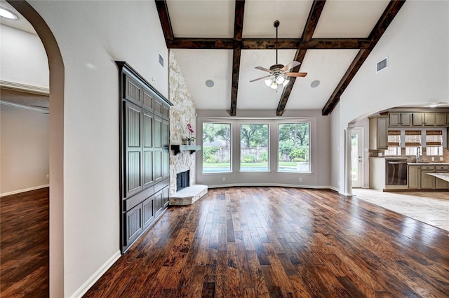 21814 Canton Pass Ln, Katy, TX 77450 - unfurnished living room with arched walkways, a ceiling fan, beamed ceiling, a stone fireplace, and a sink