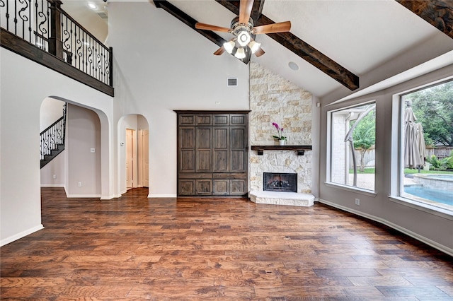 21814 Canton Pass Ln, Katy, TX 77450 - unfurnished living room featuring arched walkways, a ceiling fan, beamed ceiling, a stone fireplace, and stairs
