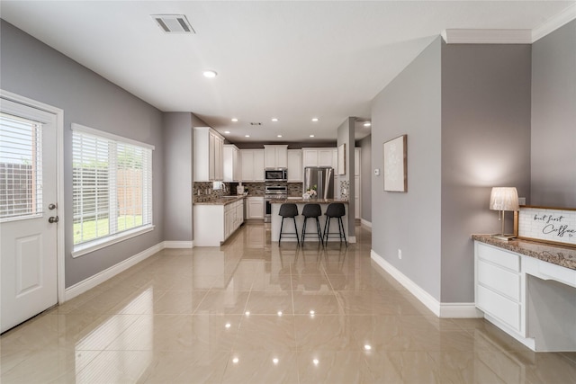 14619 Sanour Dr, Houston, TX 77084 - kitchen with stainless steel appliances, backsplash, baseboards, a kitchen bar, and white cabinetry