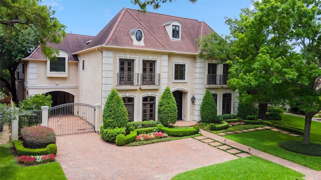 4922 Linden St, Bellaire, TX 77401 - french country inspired facade featuring a gate, a balcony, stucco siding, decorative driveway, and a shingled roof