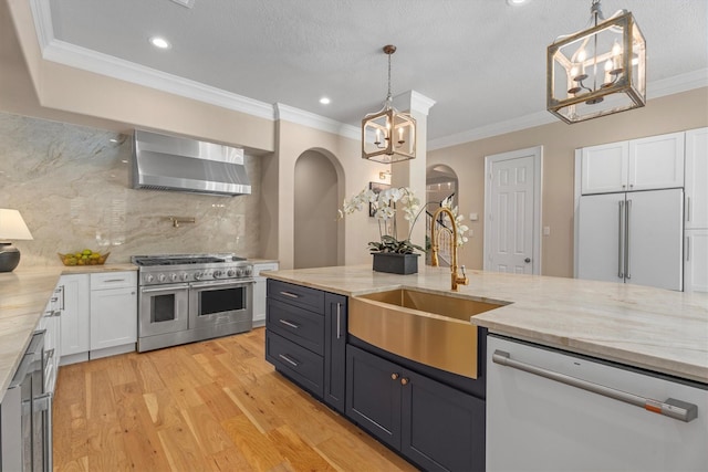 15222 Hilltop View Dr, Cypress, TX 77429 - kitchen featuring high end appliances, arched walkways, wall chimney range hood, white cabinets, and a chandelier