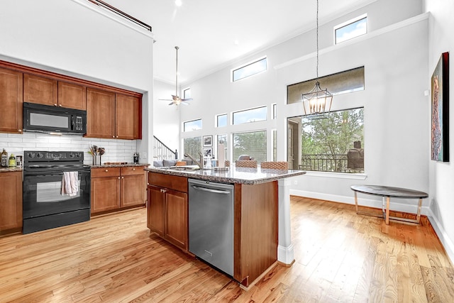 4402 Lillian St Unit 8, Houston, TX 77007 - kitchen with black appliances, dark stone countertops, brown cabinetry, light wood finished floors, and a high ceiling
