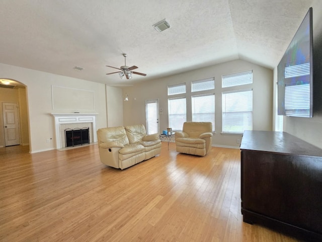17427 N Riata Lake Dr, Cypress, TX 77433 - living room featuring light wood-type flooring, a ceiling fan, arched walkways, a fireplace with flush hearth, and vaulted ceiling