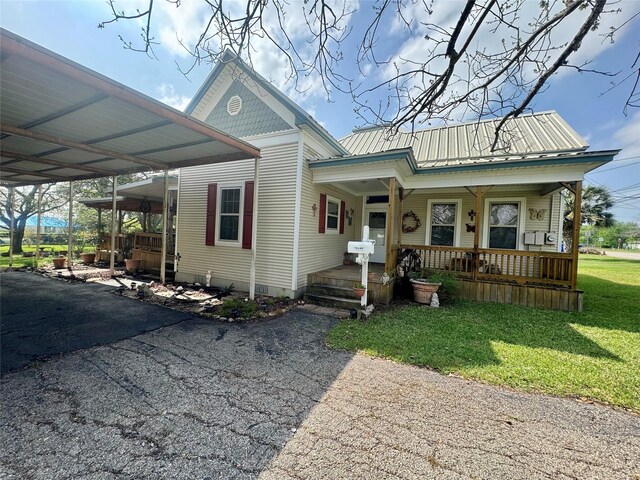 706 W St, Yoakum, TX 77995 - view of front of property featuring covered porch, a front lawn, asphalt driveway, metal roof, and a carport