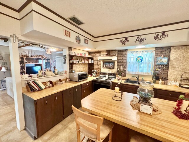 706 W St, Yoakum, TX 77995 - kitchen featuring range with gas cooktop, stainless steel microwave, a textured ceiling, dark brown cabinetry, and exhaust hood