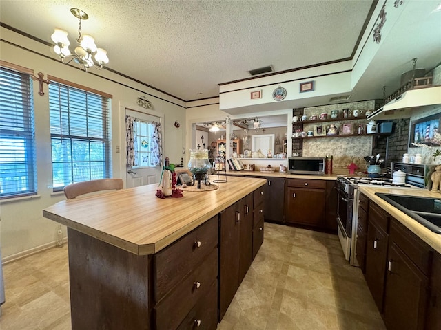 706 W St, Yoakum, TX 77995 - kitchen featuring white gas range, butcher block countertops, stainless steel microwave, dark brown cabinetry, and a chandelier