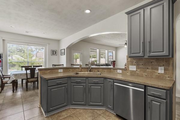 23706 River Place Dr, Katy, TX 77494 - kitchen with stainless steel dishwasher, gray cabinetry, a sink, arched walkways, and a peninsula