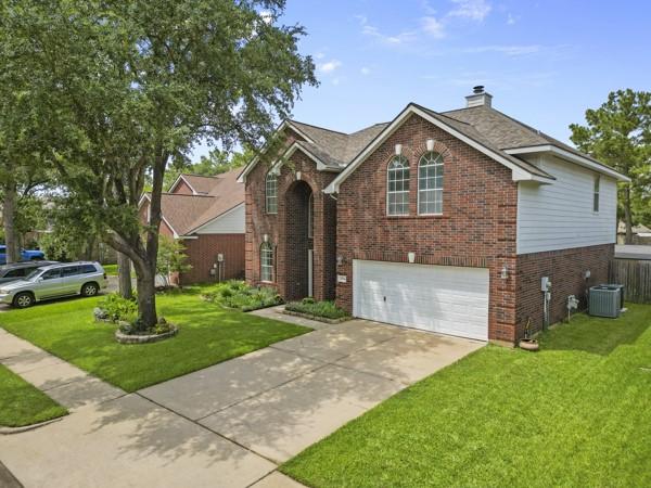 23706 River Place Dr, Katy, TX 77494 - traditional-style house featuring brick siding, a garage, a chimney, a front lawn, and cooling unit