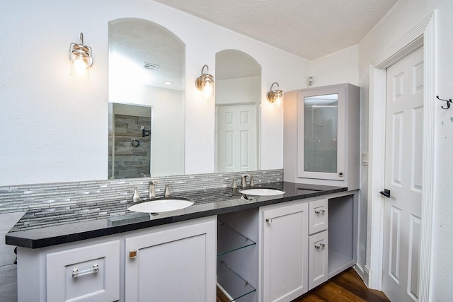 16323 Elmwood Point Ln, Sugar Land, TX 77498 - bathroom with double vanity, tasteful backsplash, a tile shower, wood finished floors, and a textured ceiling