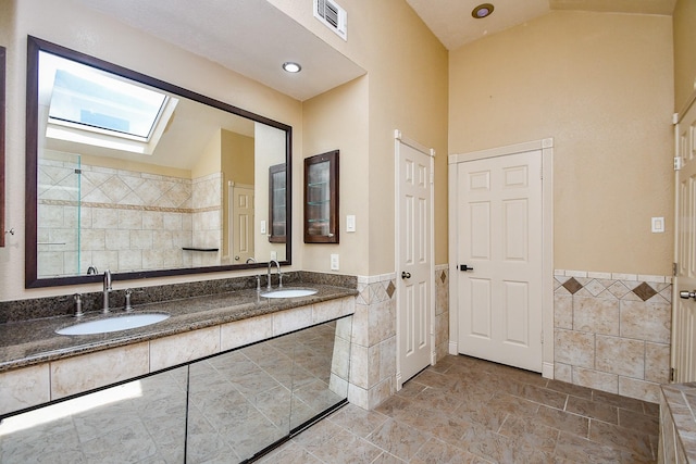 16323 Elmwood Point Ln, Sugar Land, TX 77498 - bathroom featuring tile walls, a skylight, double vanity, wainscoting, and high vaulted ceiling