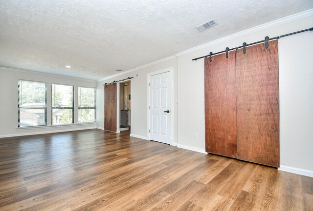 16323 Elmwood Point Ln, Sugar Land, TX 77498 - unfurnished bedroom featuring a barn door, a textured ceiling, crown molding, wood finished floors, and baseboards