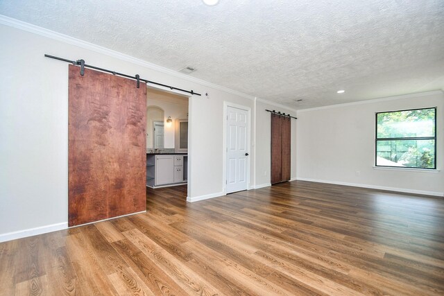16323 Elmwood Point Ln, Sugar Land, TX 77498 - spare room featuring a barn door, a textured ceiling, wood finished floors, ornamental molding, and baseboards