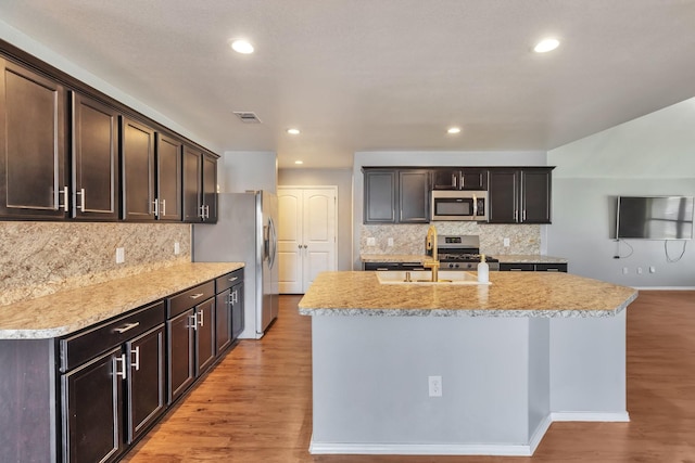 16531 Silla Ridge Ct, Houston, TX 77049 - kitchen featuring stainless steel appliances, light wood-type flooring, decorative backsplash, dark brown cabinetry, and an island with sink