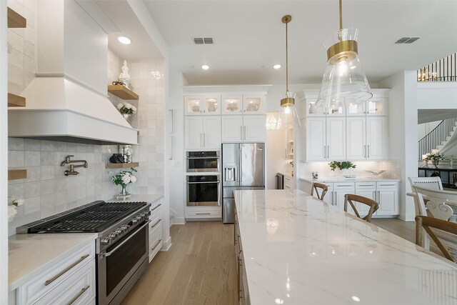 11303 Flying Admiral Dr, Cypress, TX 77433 - kitchen featuring appliances with stainless steel finishes, custom exhaust hood, light wood-style flooring, backsplash, and white cabinetry