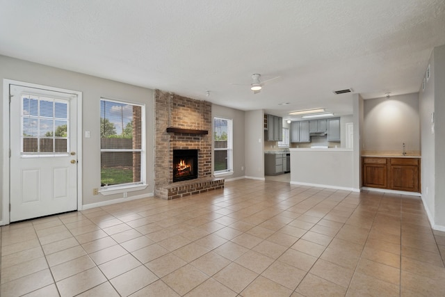 12115 Essenbruk Dr, Houston, TX 77066 - unfurnished living room featuring light tile patterned flooring, ceiling fan, a textured ceiling, a brick fireplace, and baseboards