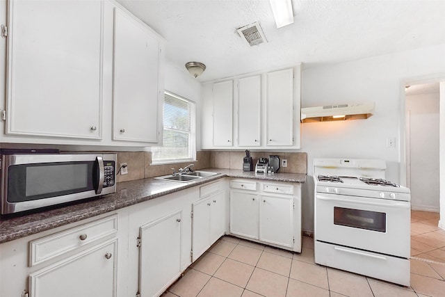 1607 Beusch Dr, Pasadena, TX 77502 - kitchen featuring stainless steel microwave, white gas stove, under cabinet range hood, light tile patterned floors, and white cabinets