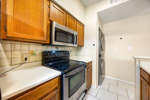 7575 Cambridge St Unit 1604, Houston, TX 77054 - kitchen with stainless steel appliances, stacked washer / drying machine, brown cabinets, decorative backsplash, and light tile patterned flooring