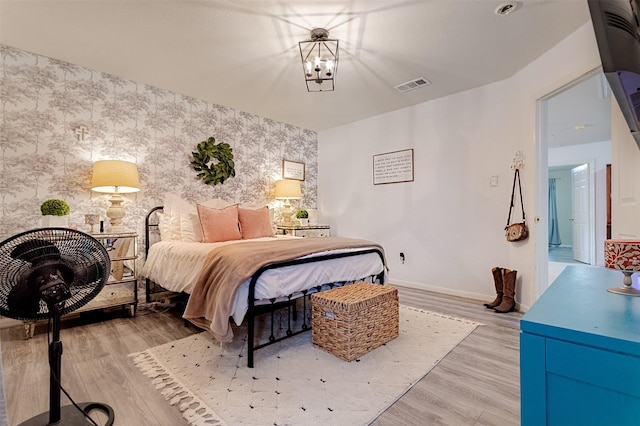 14639 Cypress Cottage Ct, Cypress, TX 77429 - bedroom featuring wallpapered walls, an accent wall, baseboards, light wood-style floors, and a chandelier