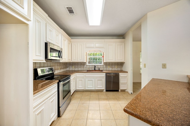 40614 Rolling Forest Dr, Magnolia, TX 77354 - kitchen featuring appliances with stainless steel finishes, a sink, tasteful backsplash, light tile patterned floors, and dark countertops