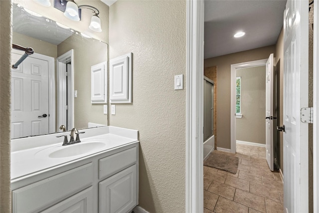 12415 Bunker Cove Dr, Cypress, TX 77433 - bathroom featuring vanity, bath / shower combo with glass door, stone finish flooring, a textured wall, and baseboards