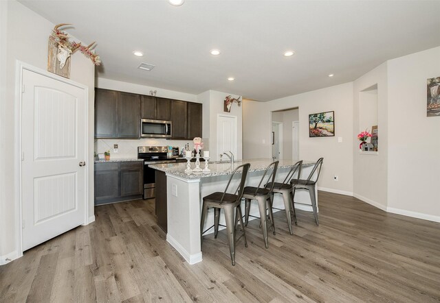 5766 Cerrillos Dr, Bryan, TX 77807 - kitchen with appliances with stainless steel finishes, light wood finished floors, a breakfast bar, a sink, and recessed lighting