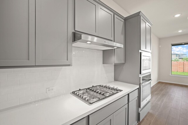 1963 Waters Branch Dr, Missouri City, TX 77459 - kitchen with stainless steel appliances, gray cabinetry, under cabinet range hood, tasteful backsplash, and recessed lighting