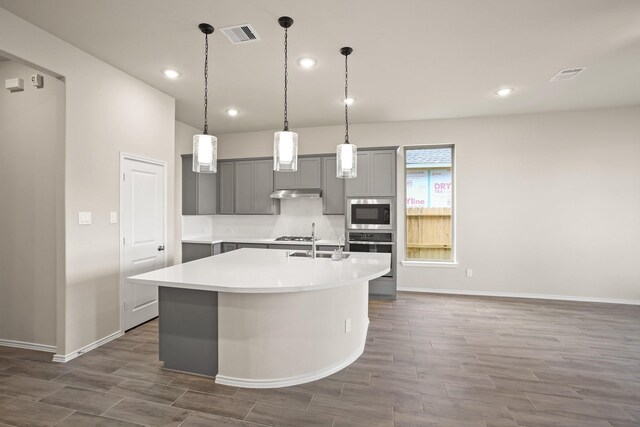 1963 Waters Branch Dr, Missouri City, TX 77459 - kitchen featuring gray cabinets, under cabinet range hood, stainless steel appliances, a kitchen island with sink, and light countertops