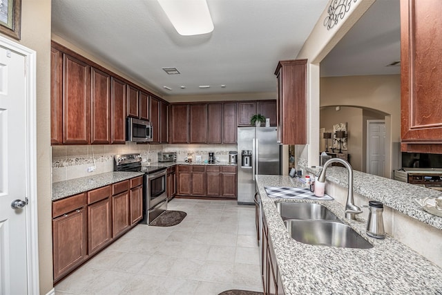 8406 Quiet Bay Dr, Baytown, TX 77523 - kitchen with appliances with stainless steel finishes, a sink, arched walkways, light stone counters, and light tile patterned floors