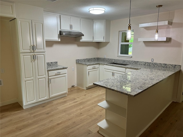 8117 Snowden St, Houston, TX 77028 - kitchen featuring open shelves, under cabinet range hood, a peninsula, light wood-style flooring, and light stone countertops