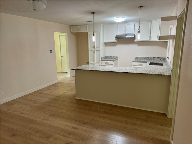 8117 Snowden St, Houston, TX 77028 - kitchen with under cabinet range hood, light wood-style floors, light stone countertops, a peninsula, and white cabinetry