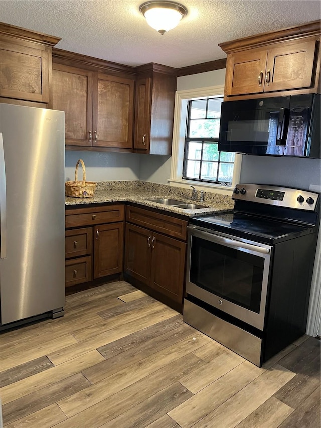 309 Aycock St, Clute, TX 77531 - kitchen with stainless steel appliances, a sink, light wood-type flooring, a textured ceiling, and light stone countertops