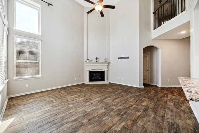 19426 Blueberry Cedar Dr, Cypress, TX 77433 - unfurnished living room featuring a towering ceiling, a ceiling fan, arched walkways, dark wood-style floors, and baseboards