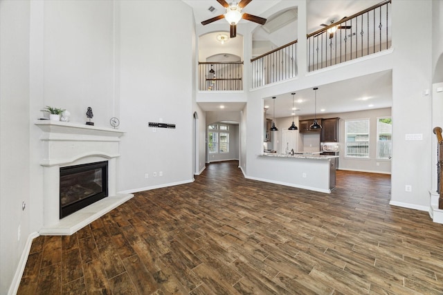 19426 Blueberry Cedar Dr, Cypress, TX 77433 - unfurnished living room with a glass covered fireplace, a ceiling fan, dark wood-style flooring, arched walkways, and baseboards
