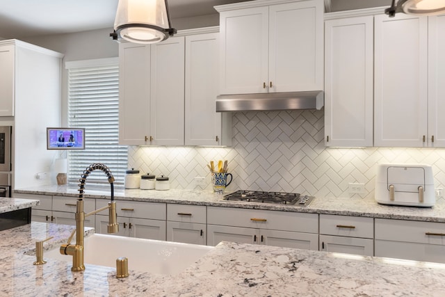 2678 Granite River Ln, Conroe, TX 77385 - kitchen with under cabinet range hood, stainless steel gas cooktop, a sink, white cabinets, and tasteful backsplash