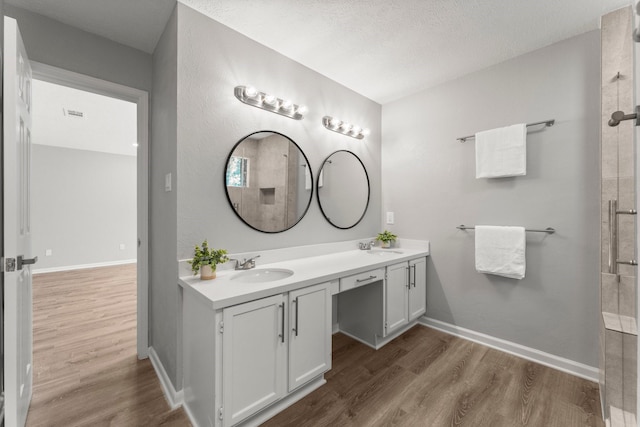 235 E Rainbow Ridge Cir, The Woodlands, TX 77381 - bathroom featuring wood finished floors, double vanity, tiled shower, and a textured ceiling