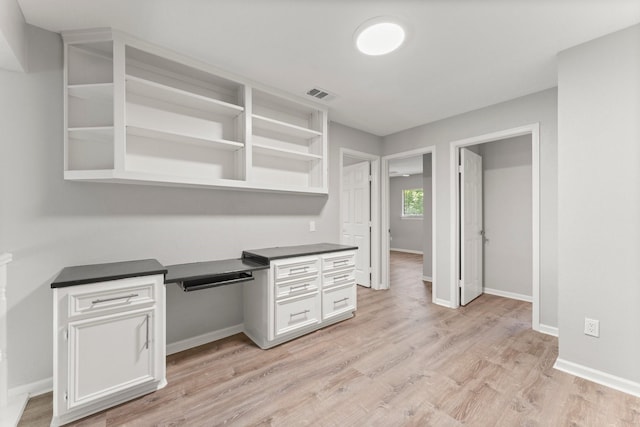 235 E Rainbow Ridge Cir, The Woodlands, TX 77381 - kitchen featuring built in desk, dark countertops, open shelves, white cabinetry, and light wood-style floors