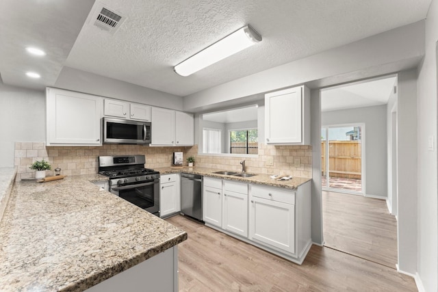 235 E Rainbow Ridge Cir, The Woodlands, TX 77381 - kitchen with appliances with stainless steel finishes, white cabinets, backsplash, light wood-style floors, and light stone counters