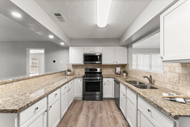 235 E Rainbow Ridge Cir, The Woodlands, TX 77381 - kitchen featuring stainless steel appliances, white cabinets, light wood finished floors, a textured ceiling, and recessed lighting