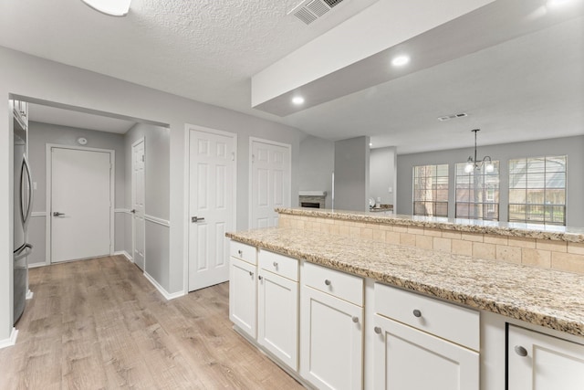235 E Rainbow Ridge Cir, The Woodlands, TX 77381 - kitchen featuring light wood finished floors, white cabinetry, a chandelier, stainless steel refrigerator, and light stone countertops