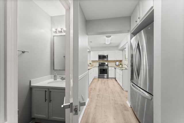 235 E Rainbow Ridge Cir, The Woodlands, TX 77381 - kitchen featuring stainless steel appliances, white cabinetry, light wood-style floors, and backsplash