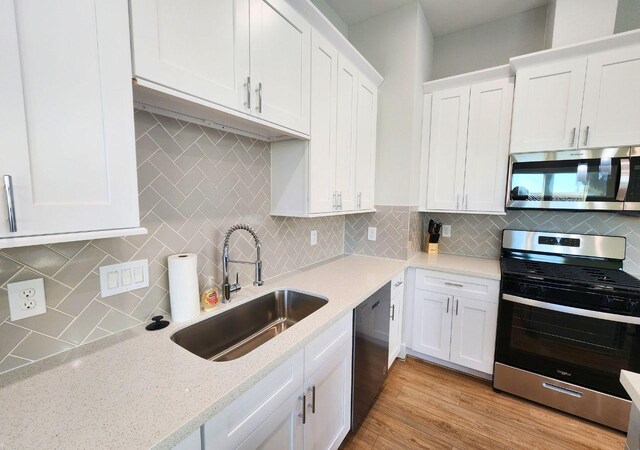 615 Northew St Unit J, Houston, TX 77091 - kitchen with appliances with stainless steel finishes, a sink, tasteful backsplash, white cabinets, and light wood finished floors