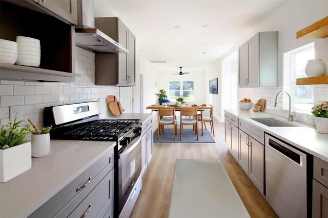 601 S Carroll St, La Porte, TX 77571 - kitchen with stainless steel appliances, a sink, wall chimney exhaust hood, light wood-type flooring, and a ceiling fan