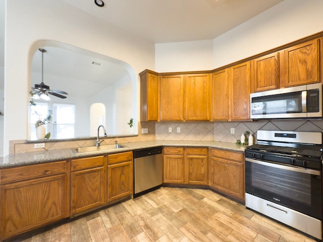4906 Arbor Falls Ln, Houston, TX 77084 - kitchen with stainless steel appliances, a sink, arched walkways, brown cabinetry, and decorative backsplash