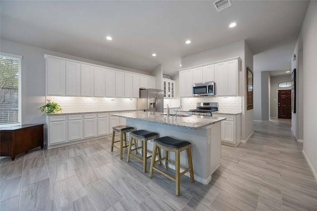 18219 Octavio Frias Trl, Houston, TX 77044 - kitchen with stainless steel appliances, a kitchen island with sink, decorative backsplash, white cabinets, and light stone countertops