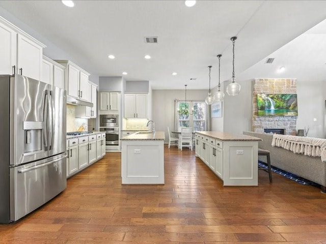 17806 Creek Bluff Ln, Cypress, TX 77433 - kitchen featuring appliances with stainless steel finishes, a center island with sink, under cabinet range hood, open floor plan, and white cabinetry
