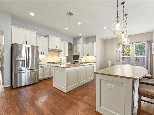 17806 Creek Bluff Ln, Cypress, TX 77433 - kitchen featuring appliances with stainless steel finishes, a center island with sink, under cabinet range hood, tasteful backsplash, and recessed lighting